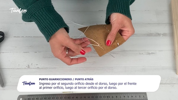Lección en video del curso de marroquinería de Tanten: manos cosiendo cuero a mano, con el subtítulo explicando el paso y el logo de la escuela