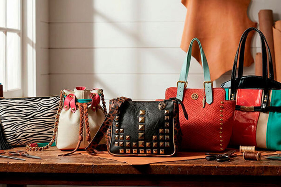Cinco carteras y bolsos de cuero hechos a mano sobre una mesa de taller de marroquinería