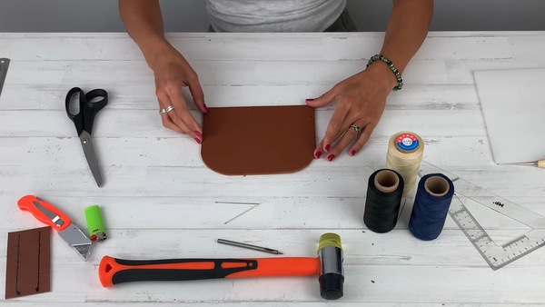 Kit de herramientas para marroquinería: tijera, cutter, mazo de goma, hilo encerado, agujas y escuadra sobre la mesa